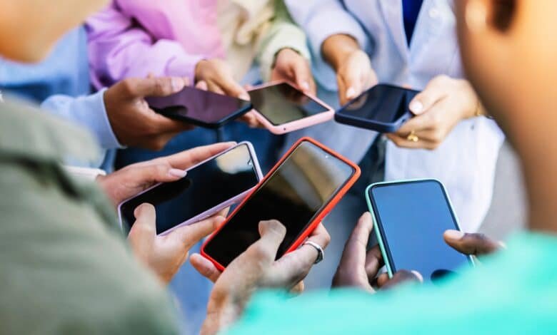 Photo: Young group of people standing in the circle using mobile phones outside.